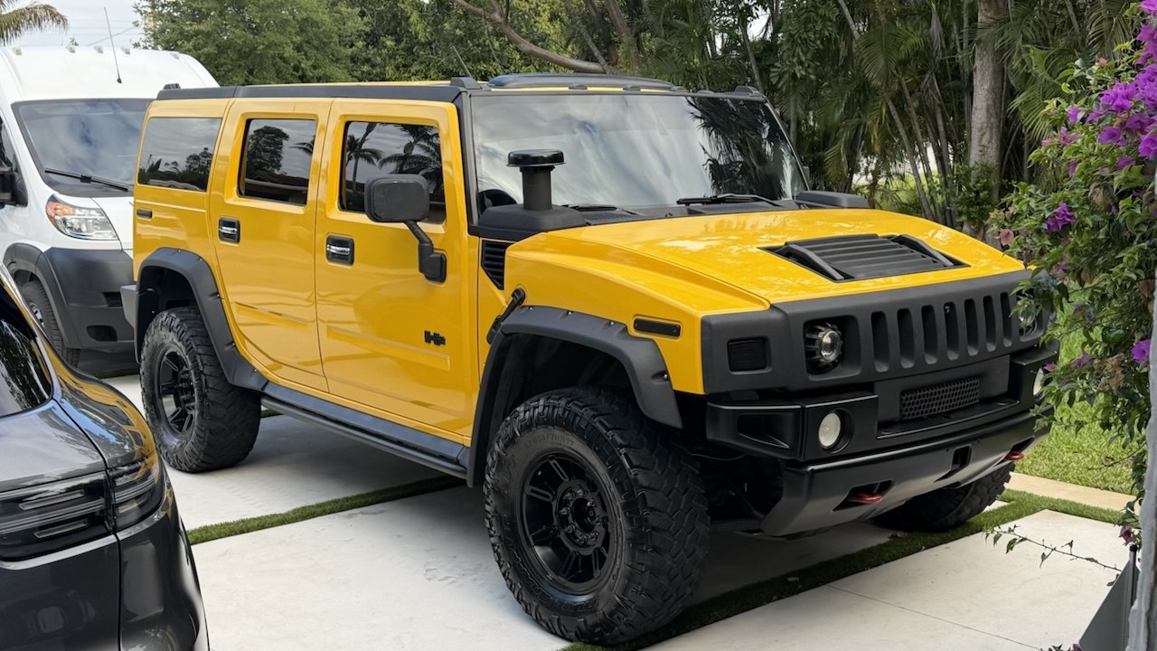 Bright yellow Hummer H2 parked in a tropical driveway, the Thursday taco dream machine.
